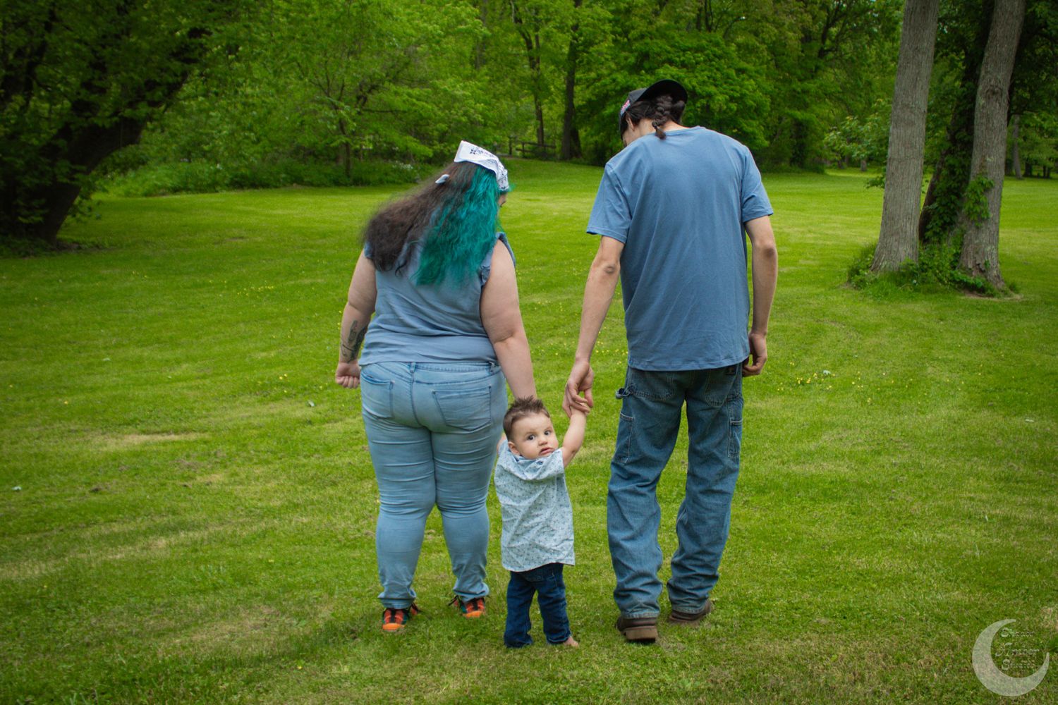 A family walks together on a lush green lawn in a park setting during a sunny day.