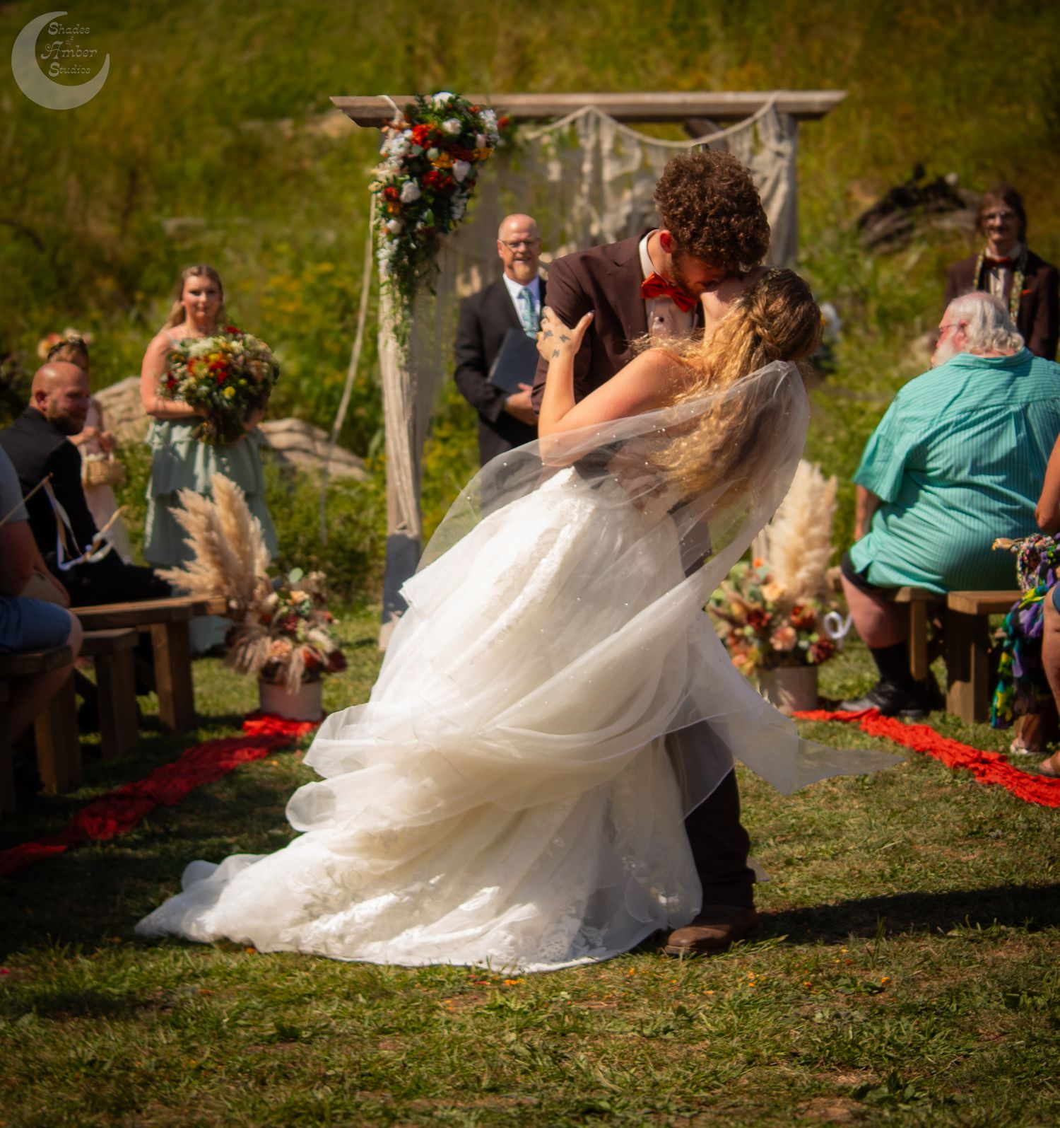 Wedding ceremony outdoors with guests seated on wooden benches and rose petals scattered along the aisle.