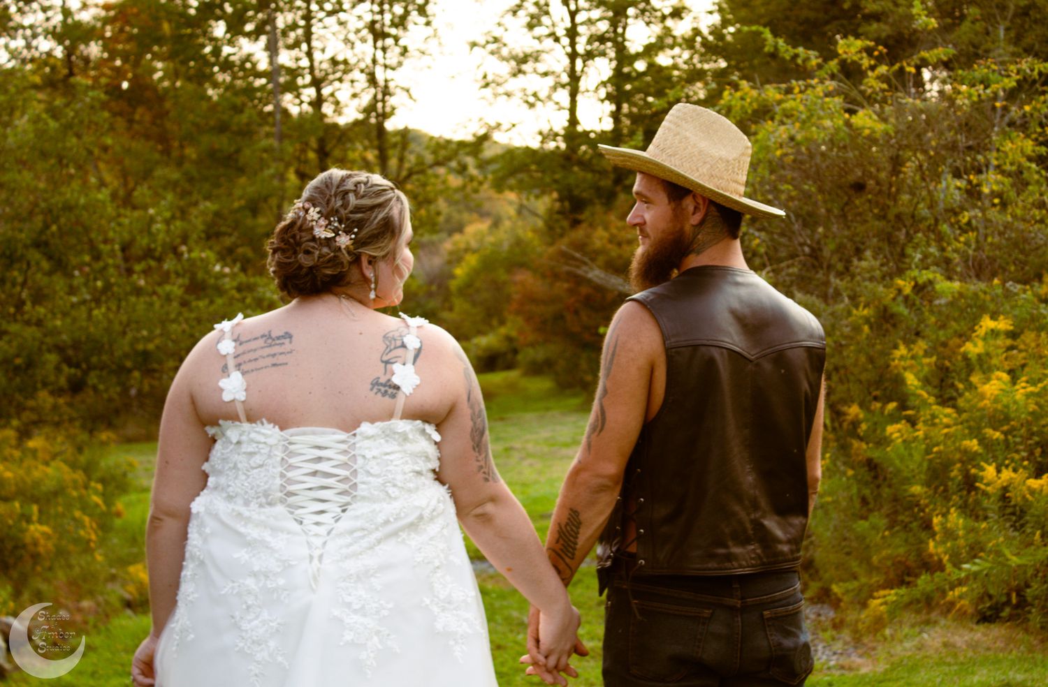 A couple holding hands while walking through a sunlit garden on their wedding day.