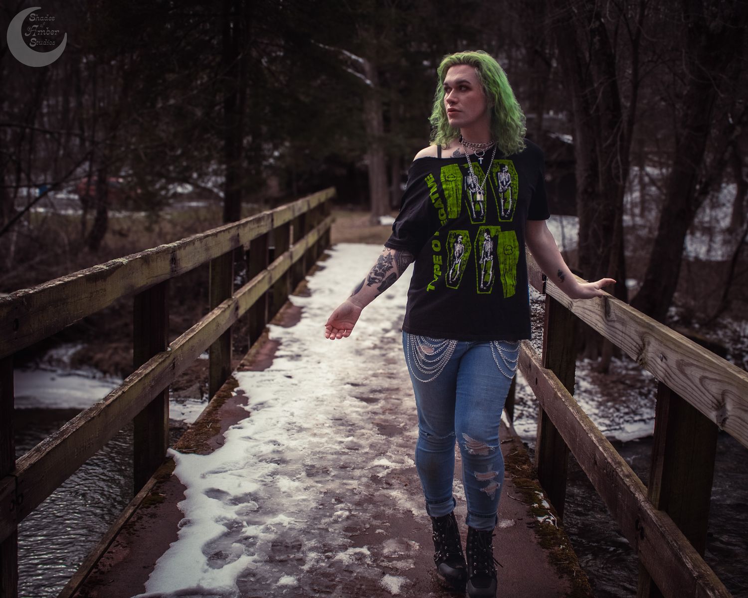 A figure with bright green hair walks on a snowy wooden bridge path through a winter forest.
