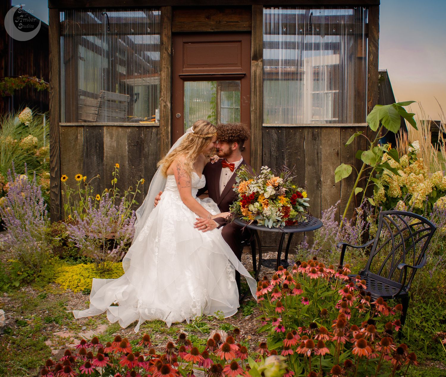 A romantic garden wedding scene shows a couple sitting among vibrant red flowers and lush greenery at sunset.