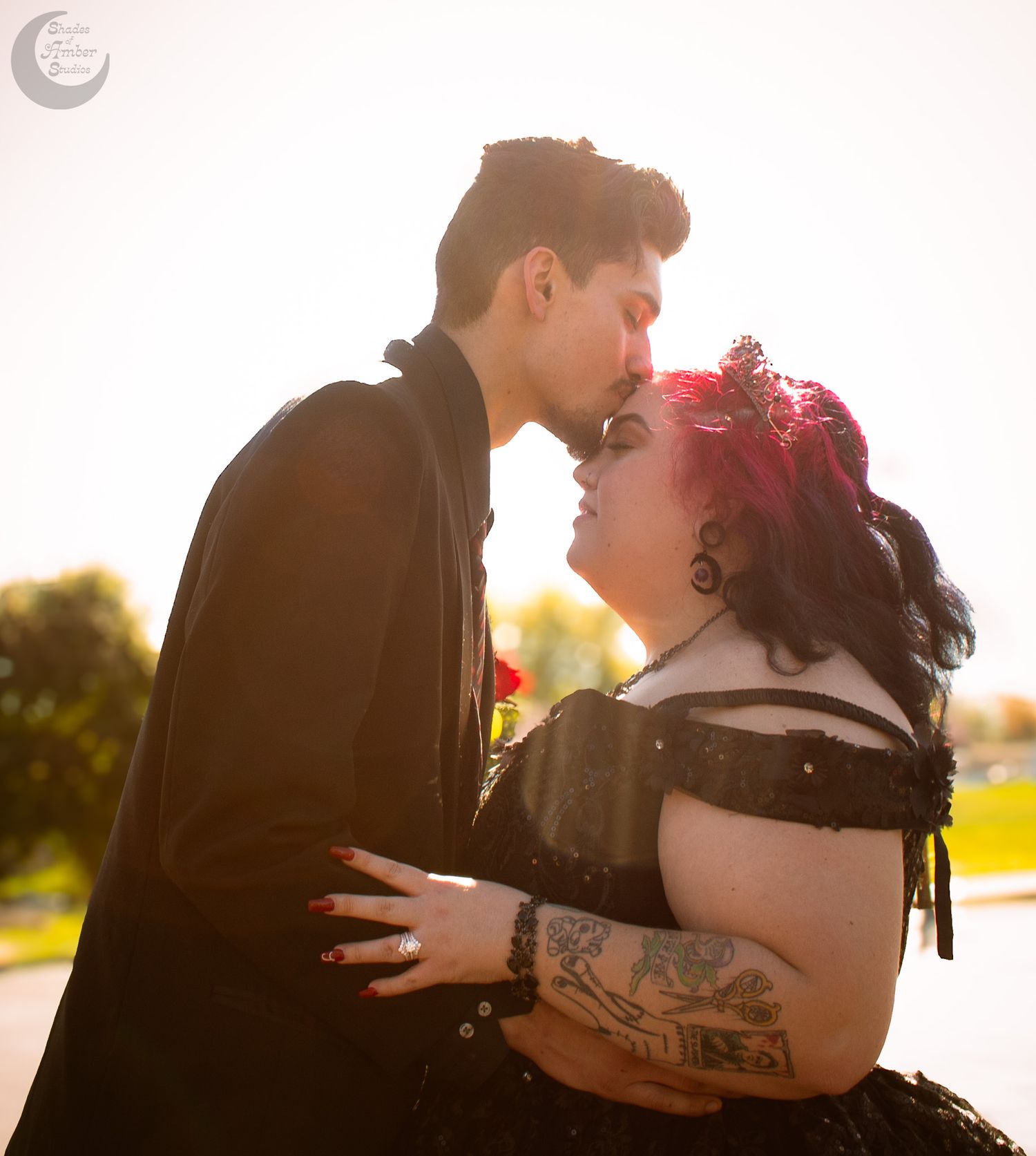 Romantic couple embraces in a warm sunset glow with pink flowers and tattoo details visible.