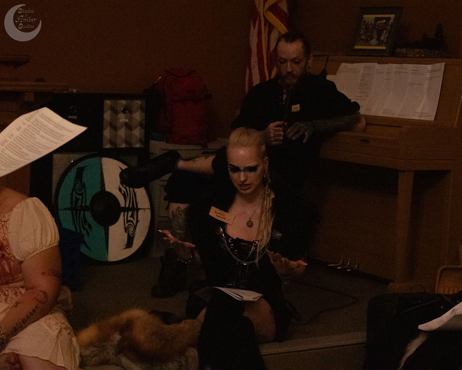 Musicians in dark leather and gothic attire rehearse in a dimly lit room with instruments and sheet music.