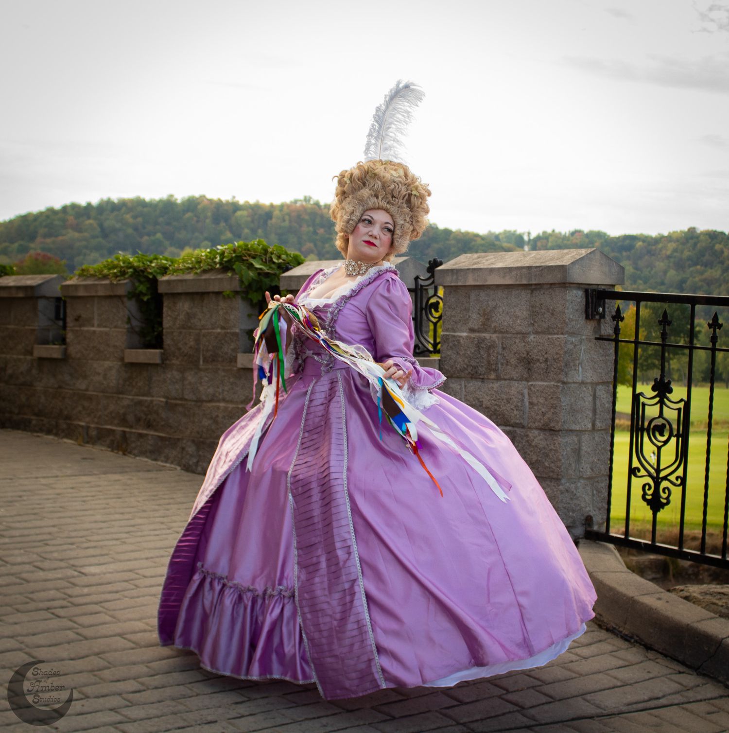 Person in ornate purple Victorian ballgown poses dramatically on castle terrace.
