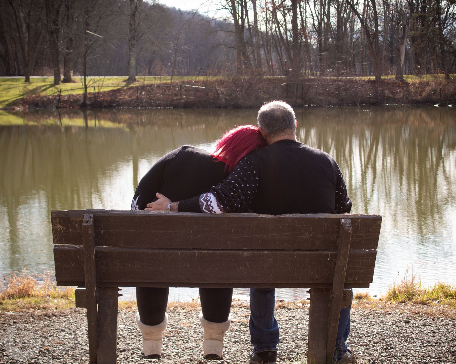 Four silhouettes sitting on wooden benches by a serene lake at dusk create a peaceful outdoor scene.