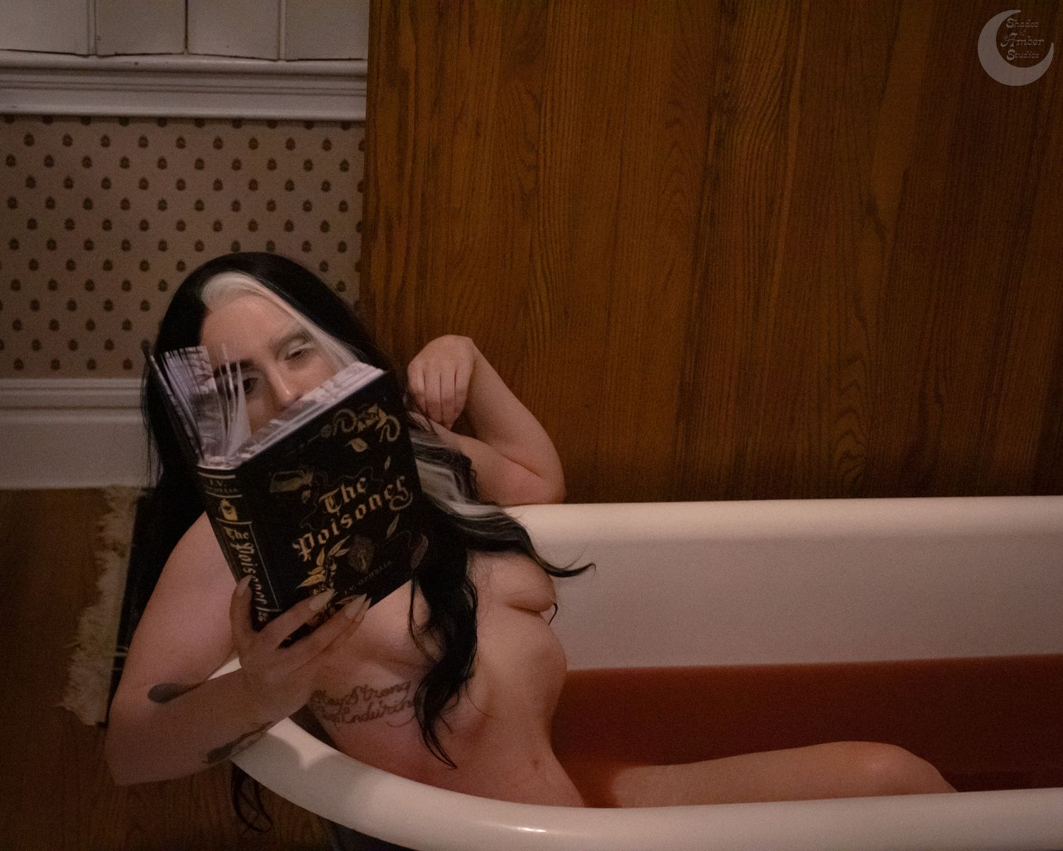 Person relaxing in a clawfoot bathtub reading a book titled The Dungeon in a wood-paneled bathroom.