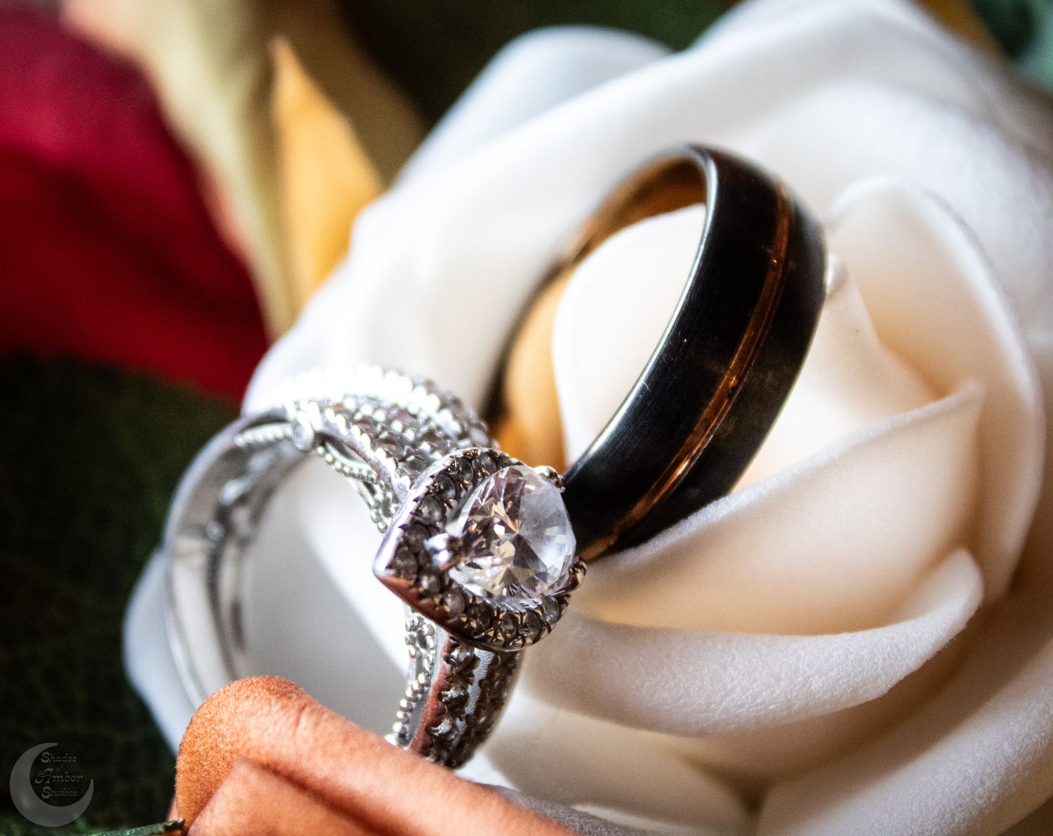 Wedding rings nestled in a white rose, featuring a sparkling diamond engagement ring.