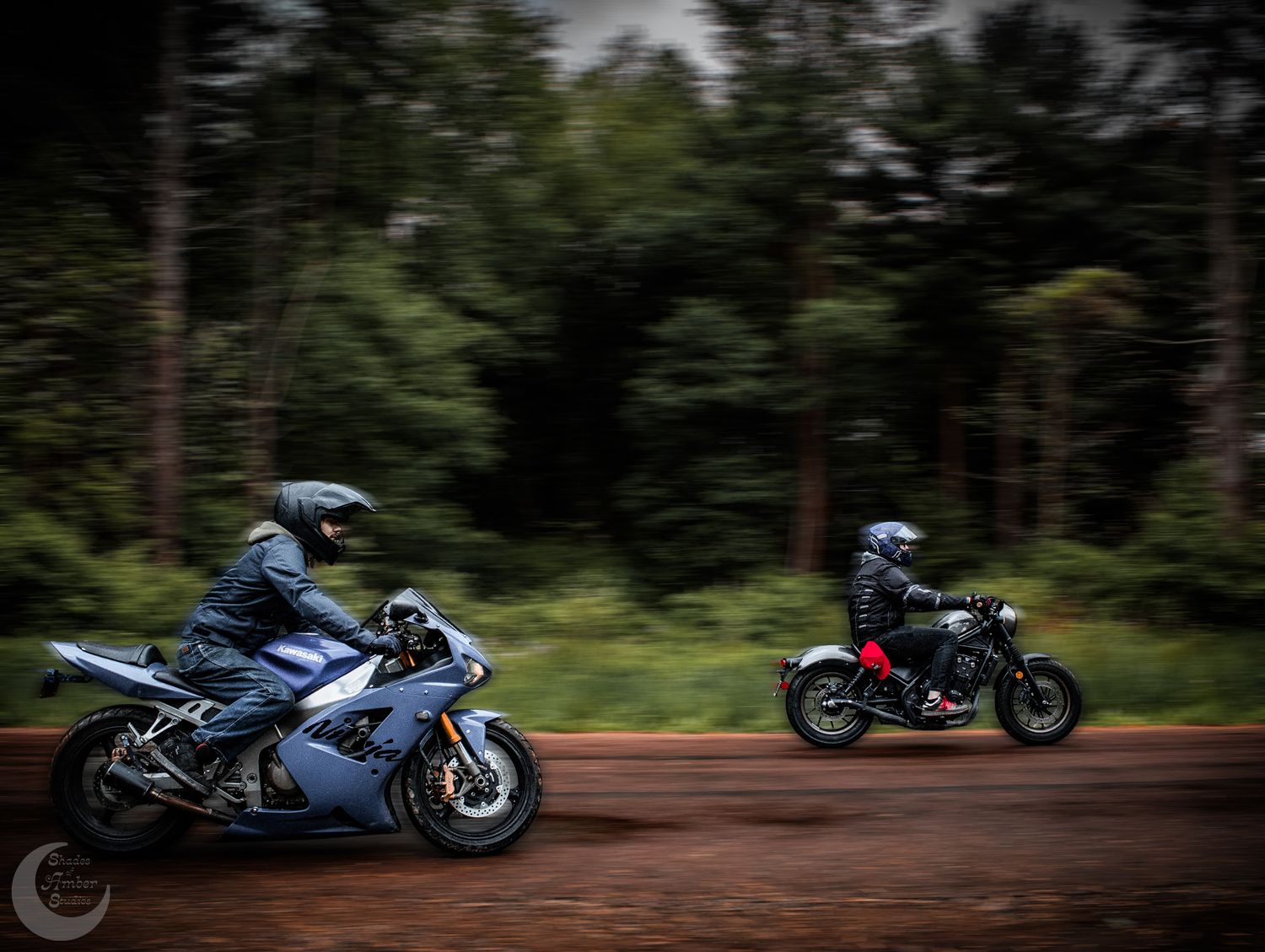 Two motorcyclists racing on sport bikes through a forested road with motion blur effect.