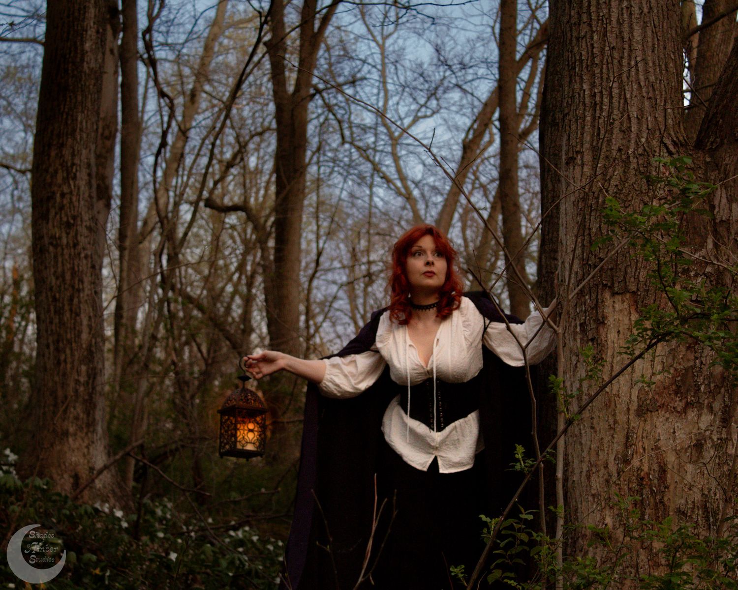 A person holds a lantern while wearing period clothing and cape in a misty forest setting.