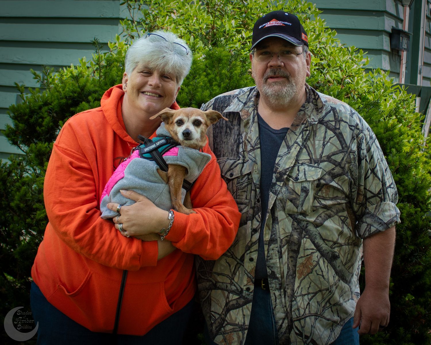 A group of people in orange and camouflage clothing gather outdoors with small dogs in their arms.