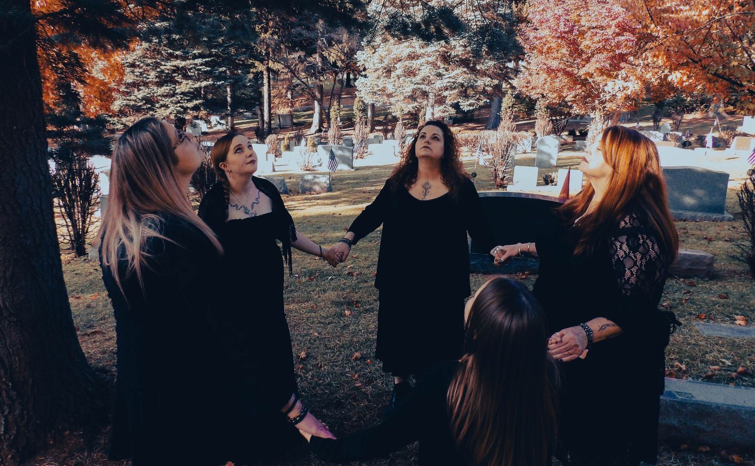 Group in black dresses standing together outdoors in autumn setting.