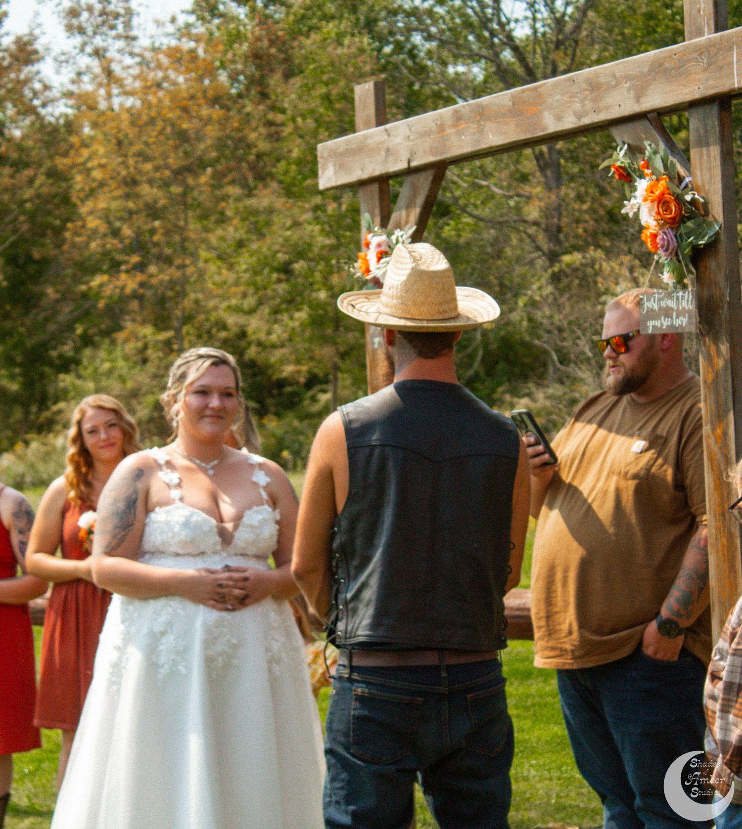 Outdoor wedding ceremony under wooden arch with fall floral decorations.