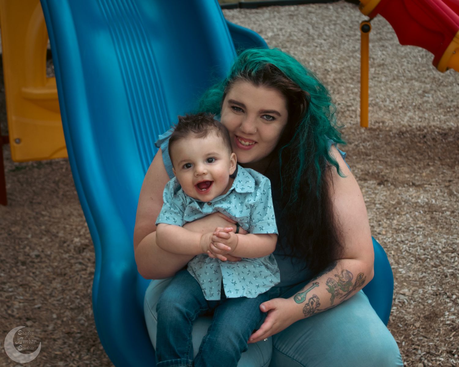 Child laughing while playing on a bright blue playground slide with adult assistance.
