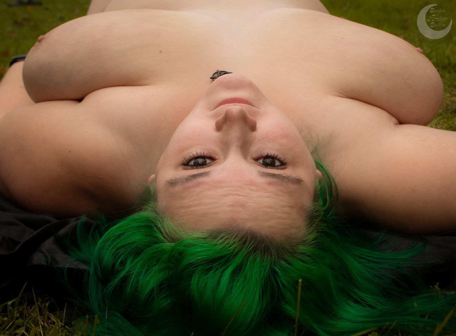 Person with bright green hair lying on grass in artistic outdoor portrait.