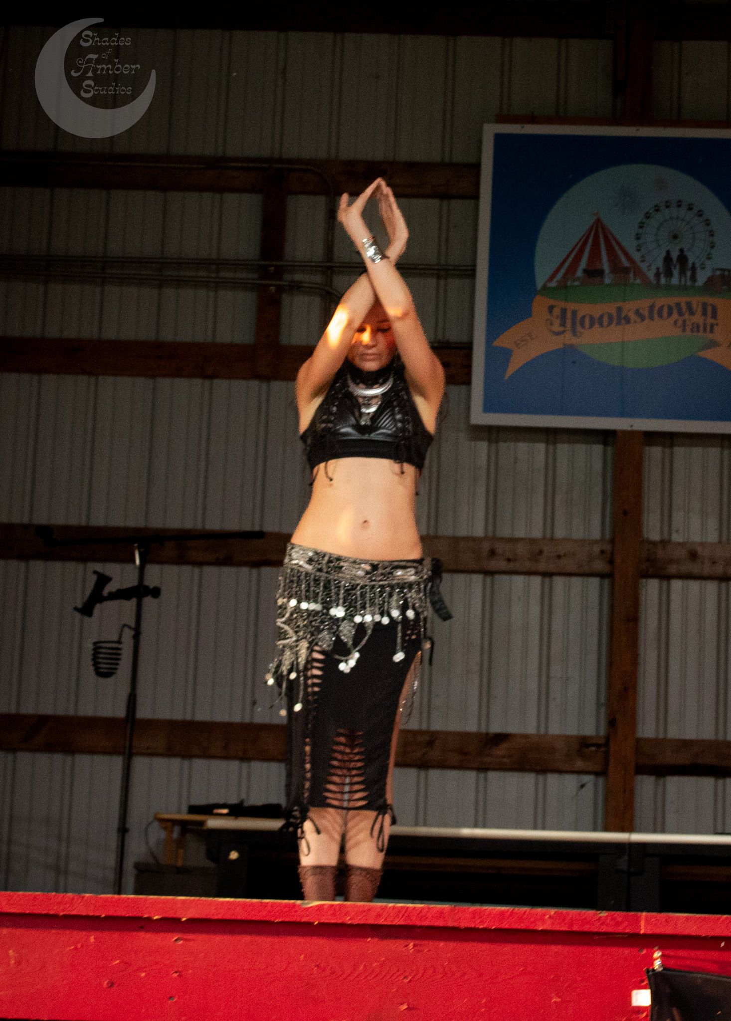 A person in black workout attire performs a split leap jump on a low red gymnastics beam during practice.