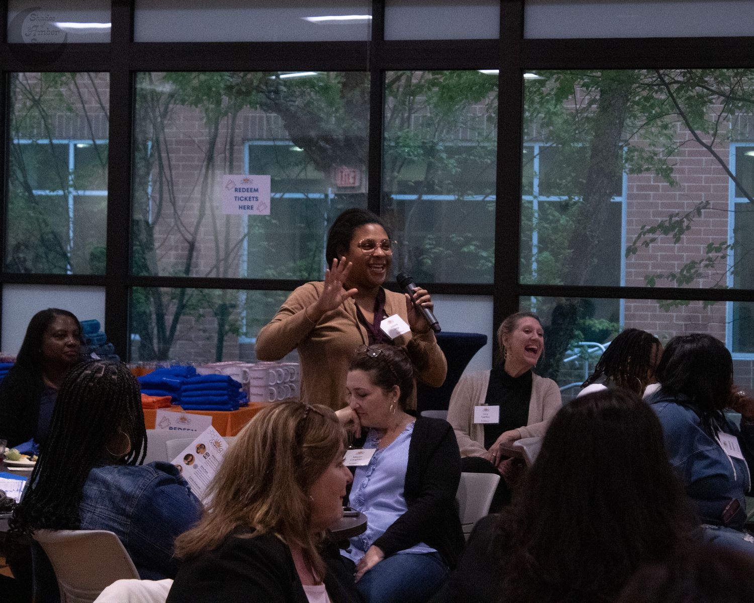 Students gather in a classroom as someone stands and speaks at a casual indoor meeting or discussion group.