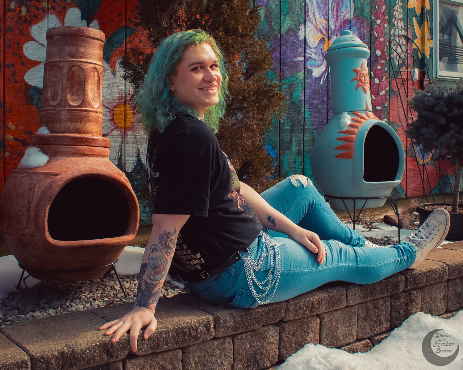 Relaxed pose by decorative garden chimineas against colorful mural wall.
