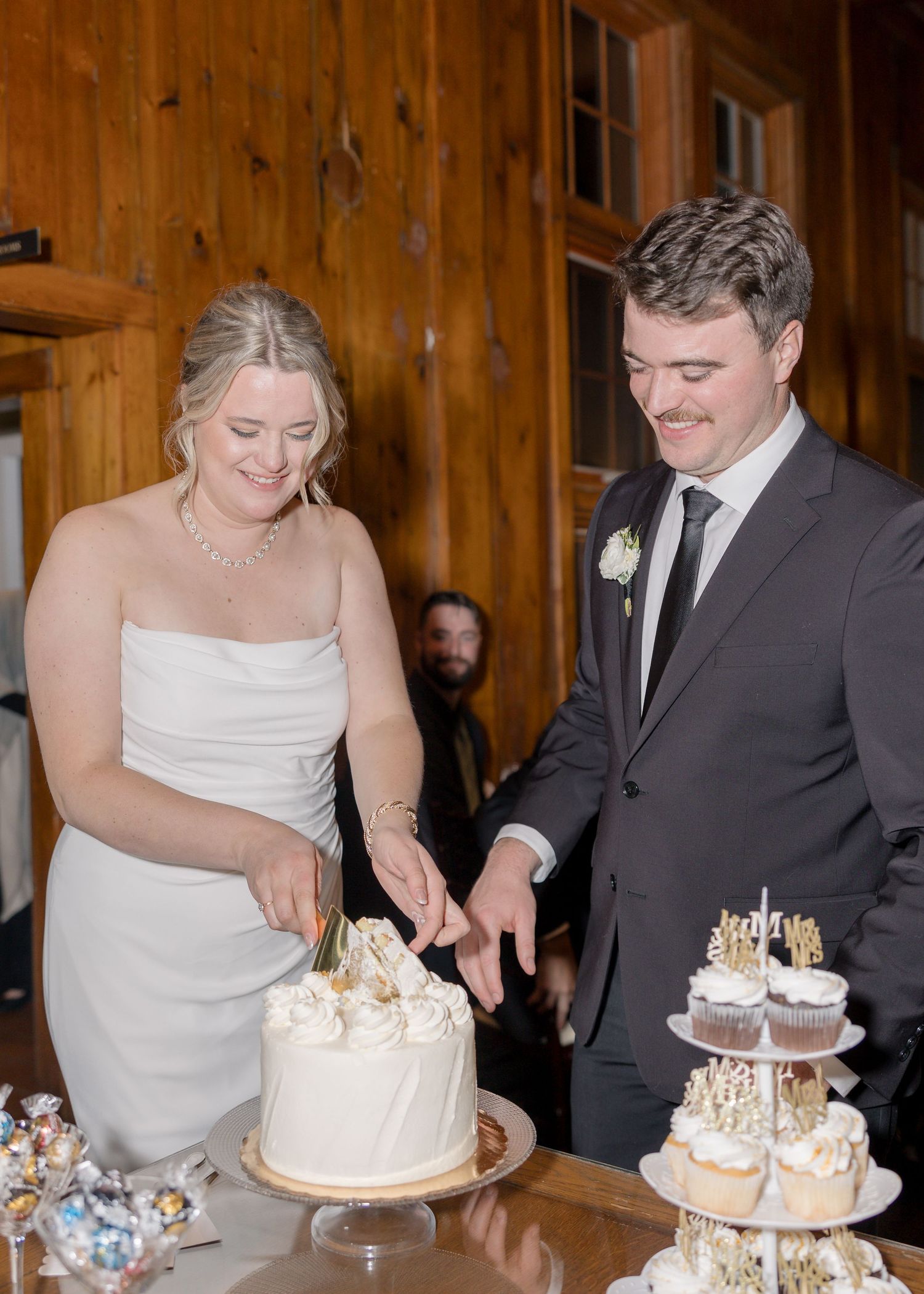 Wedding cake cutting moment in a wooden-paneled reception venue.