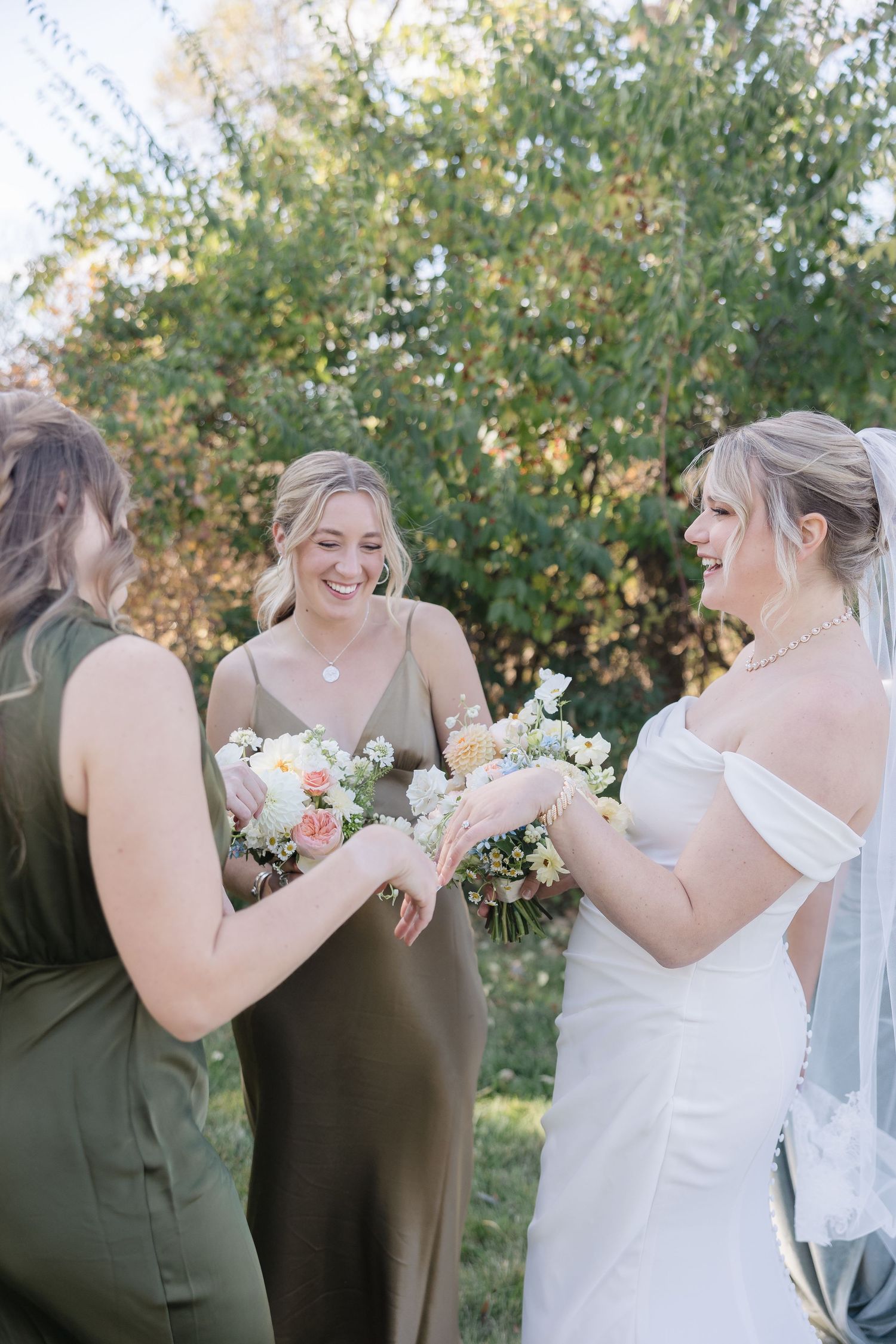 Bridesmaids share a joyful moment with bouquets during an outdoor wedding celebration.