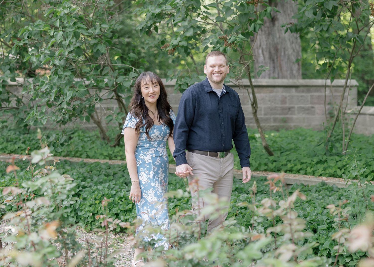 A couple walks hand in hand through lush green gardens during their outdoor photo session.