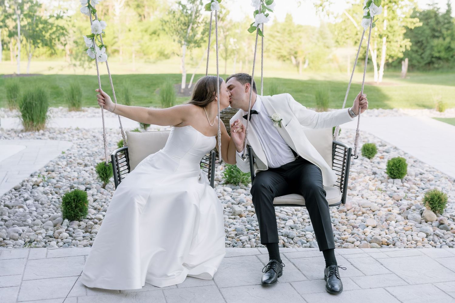 Bride and groom kissing on a decorative swing surrounded by lush greenery on their wedding day.