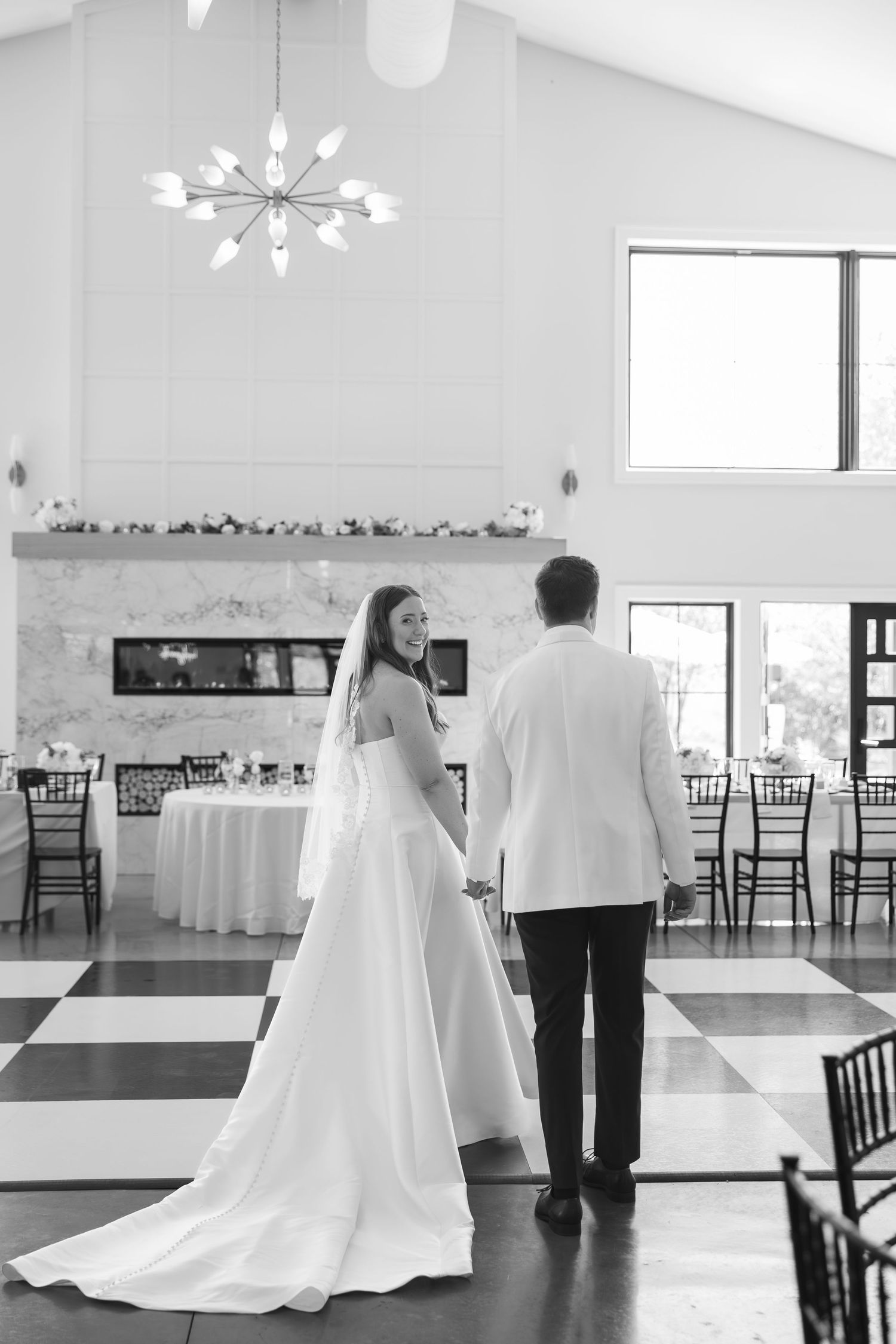 Bride and groom hold hands on checkered dance floor in elegant black and white wedding reception venue.
