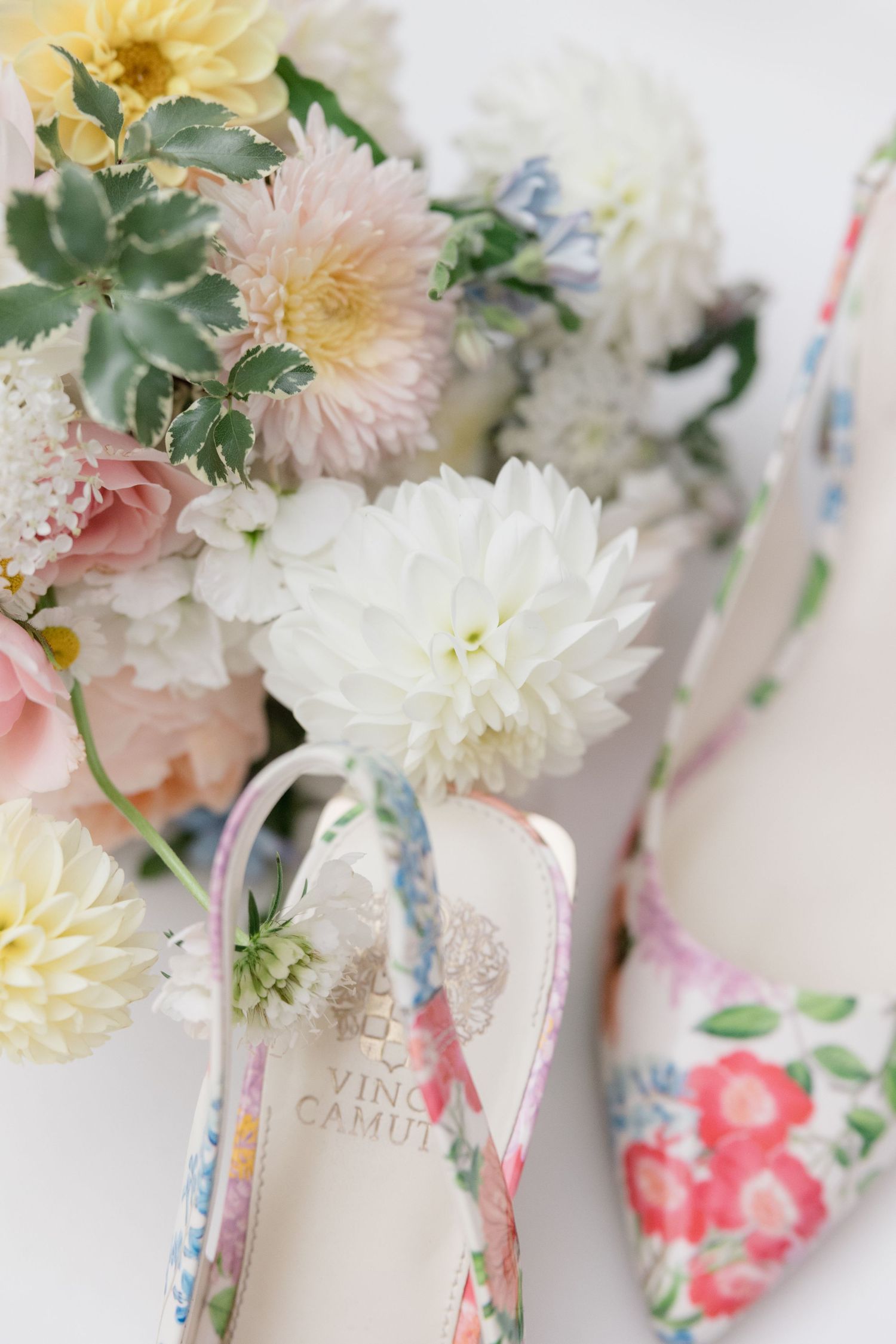 Pastel flowers arranged with floral print shoes in soft dreamy wedding detail shot.