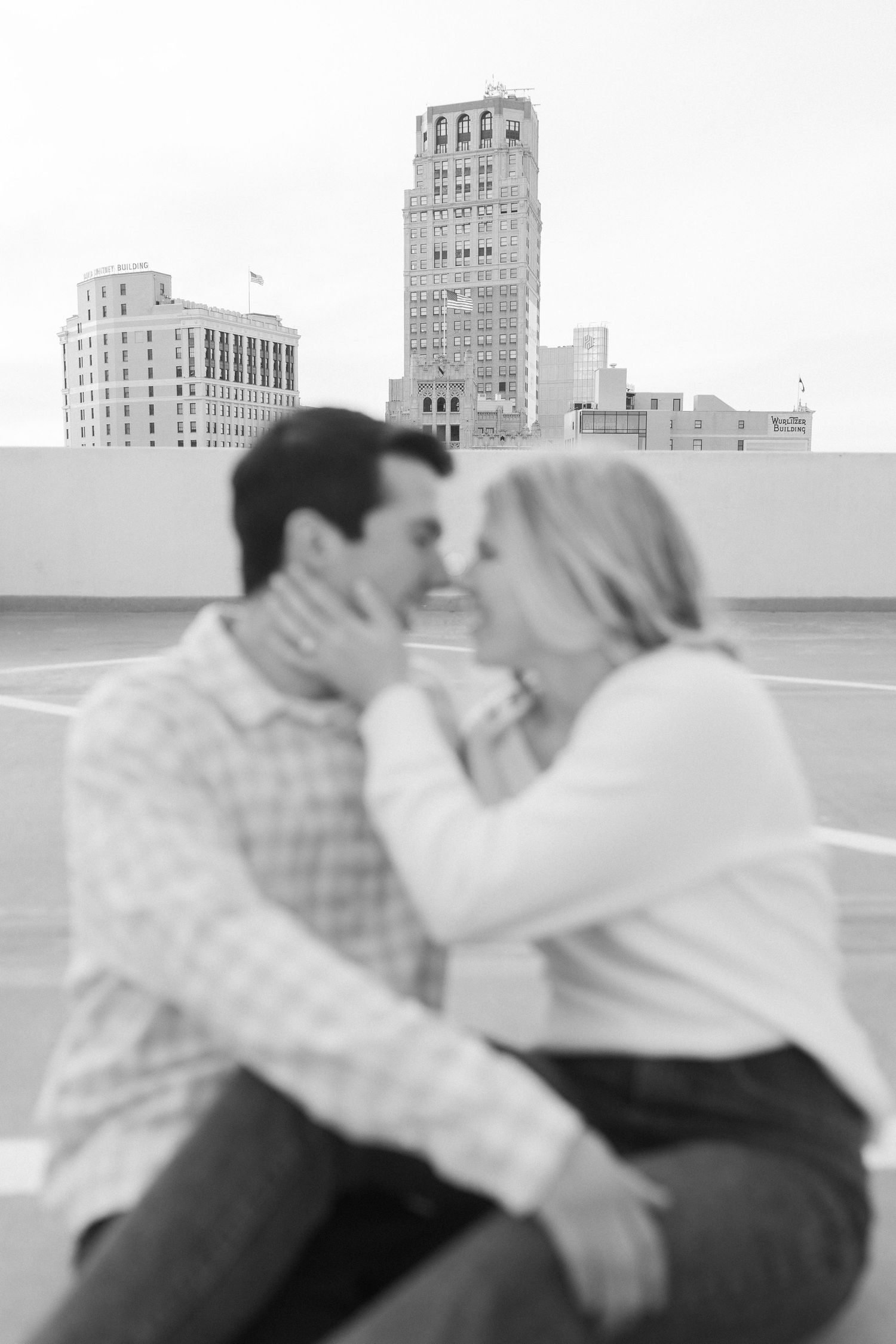A black and white photo capturing an intimate moment on a rooftop with art deco buildings in the background.