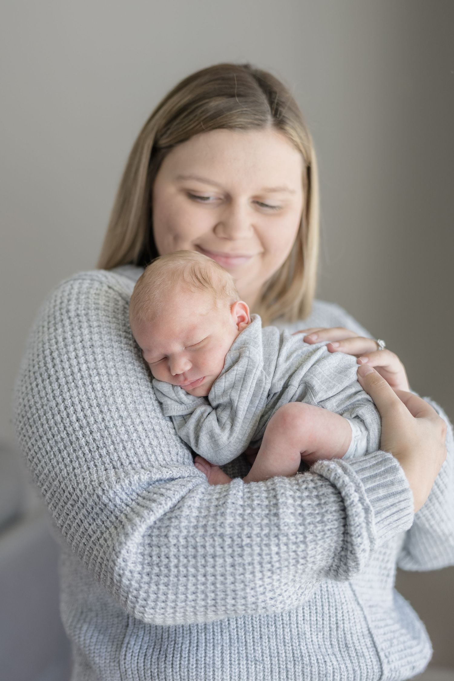 A tender moment captured in a series of photos showing a parent cradling a sleeping baby in soft grey knitwear.