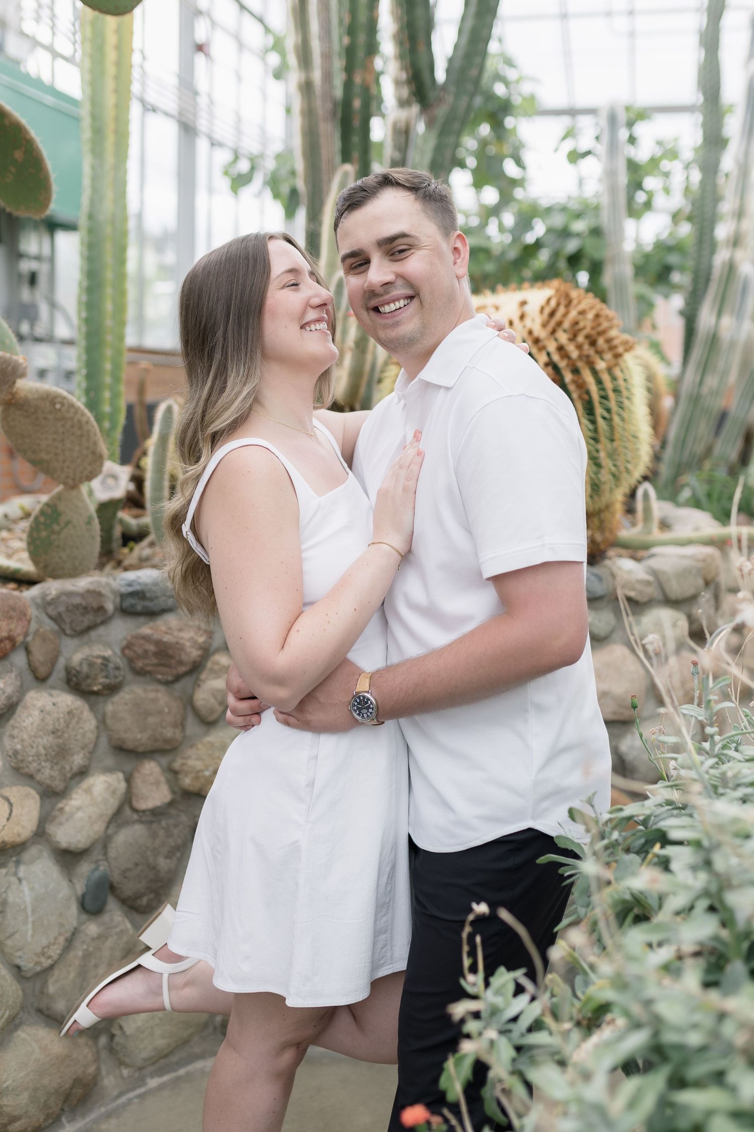 A couple shares a joyful moment together in a greenhouse filled with cacti and stone walls.