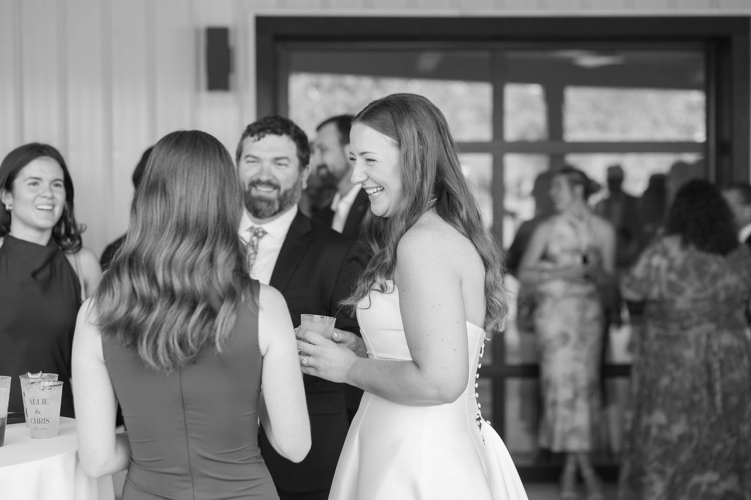 A joyful bride laughs with guests during her wedding reception in a bright elegant venue.