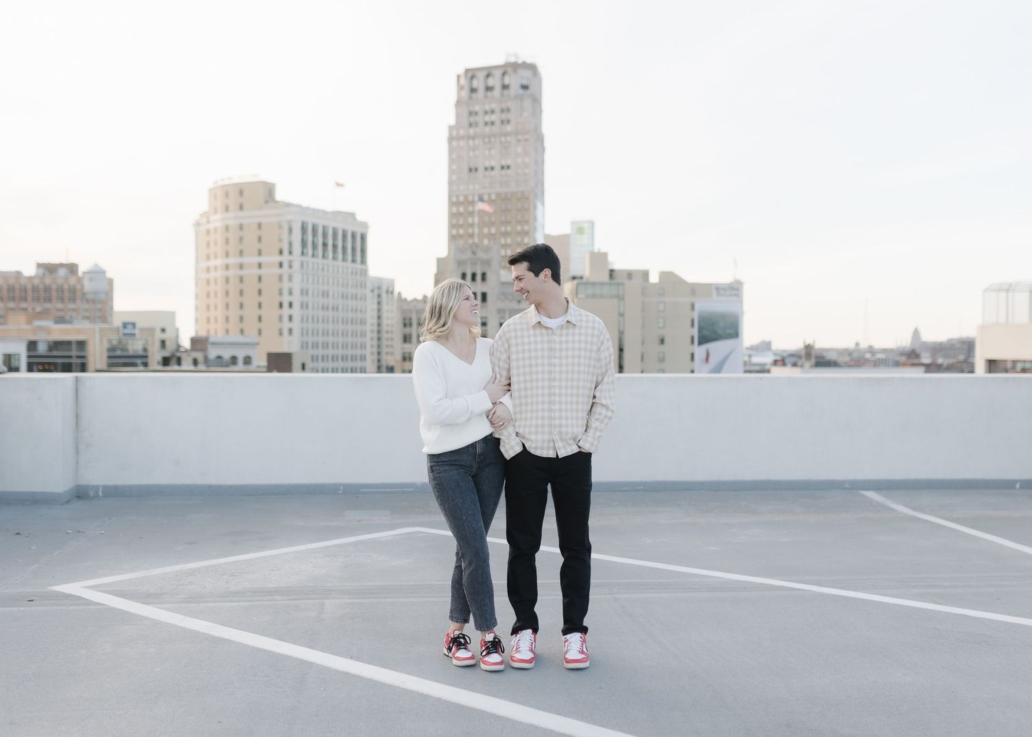 A couple stands together on a rooftop overlooking a city skyline.