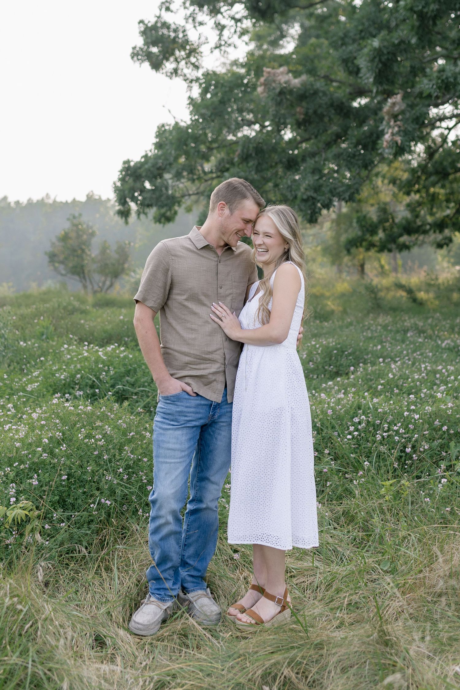 A romantic couple embraces in a wildflower meadow wearing casual summer outfits during a sunny afternoon photoshoot.
