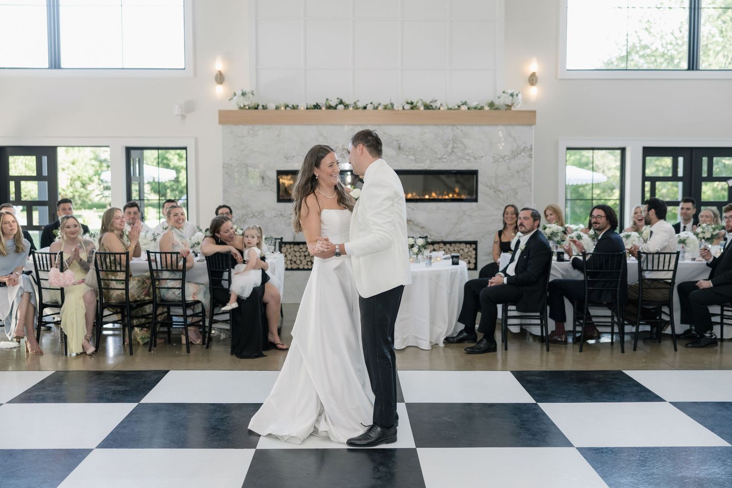 Bride and groom share first dance on black and white checkered floor at elegant wedding reception.