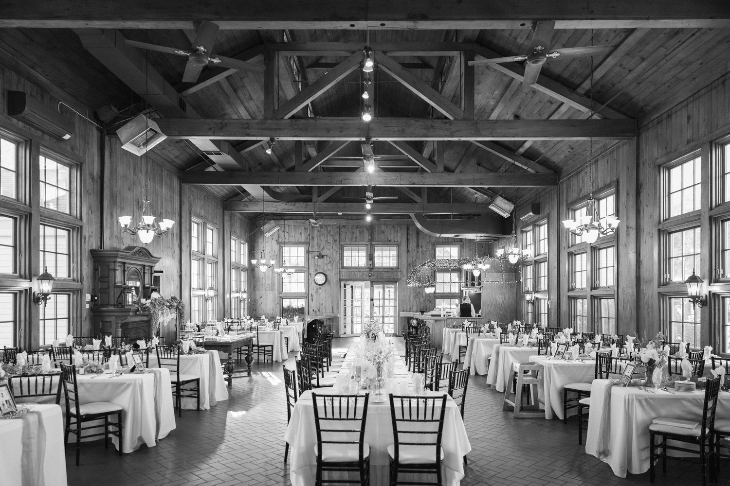 Elegant wedding reception venue with exposed wooden beams, white tablecloths, and natural lighting through large windows.