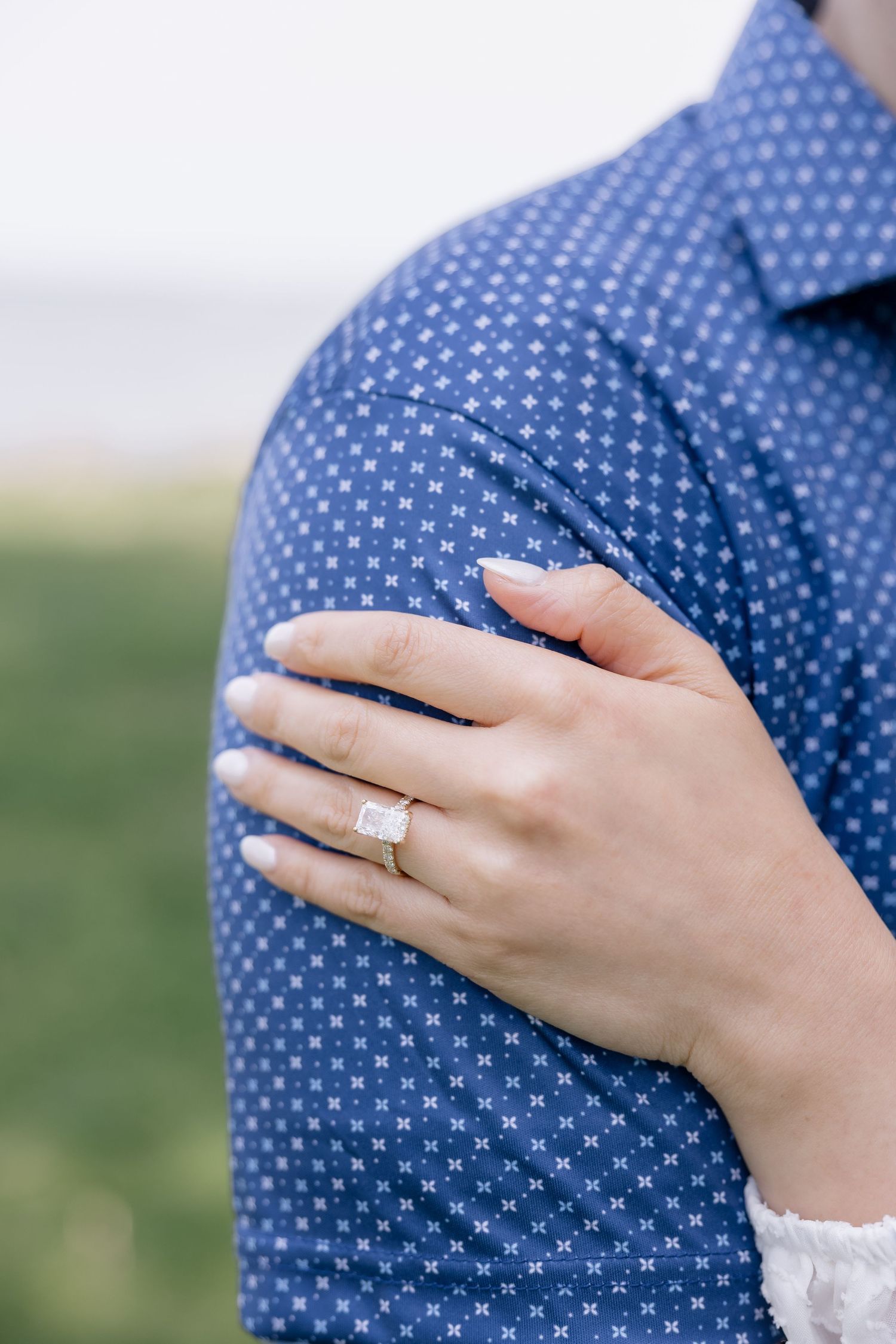 Close up of person's hand wearing a gold wedding ring against a navy blue polka dot shirt.