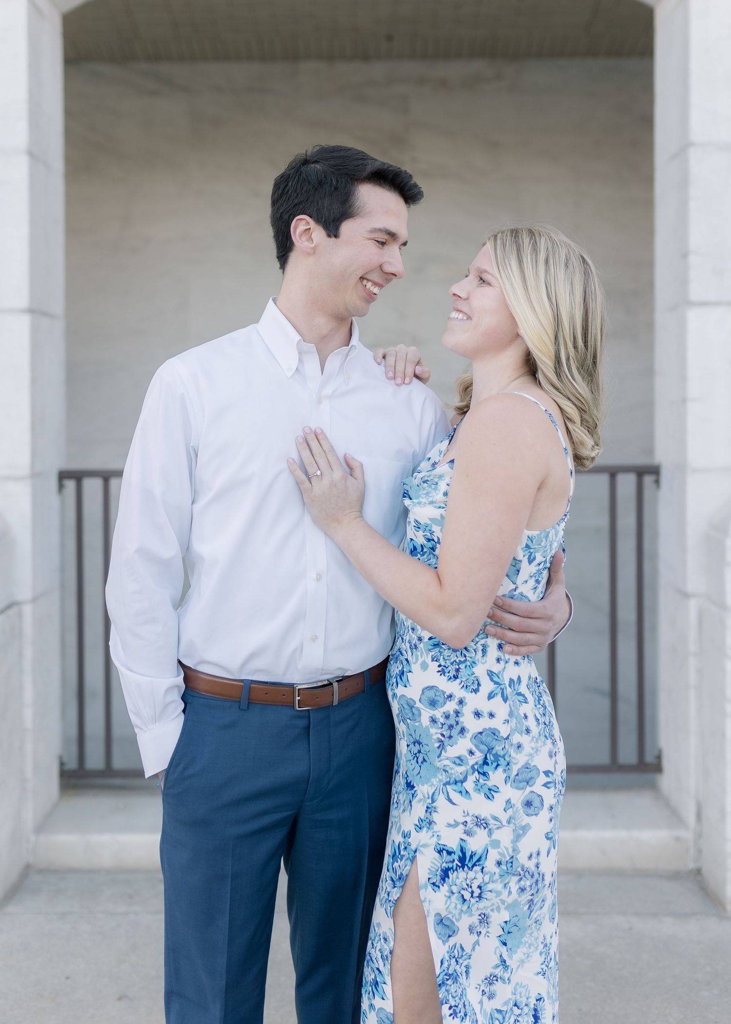 A romantic couple shares a joyful moment together in formal attire against a light architectural background.