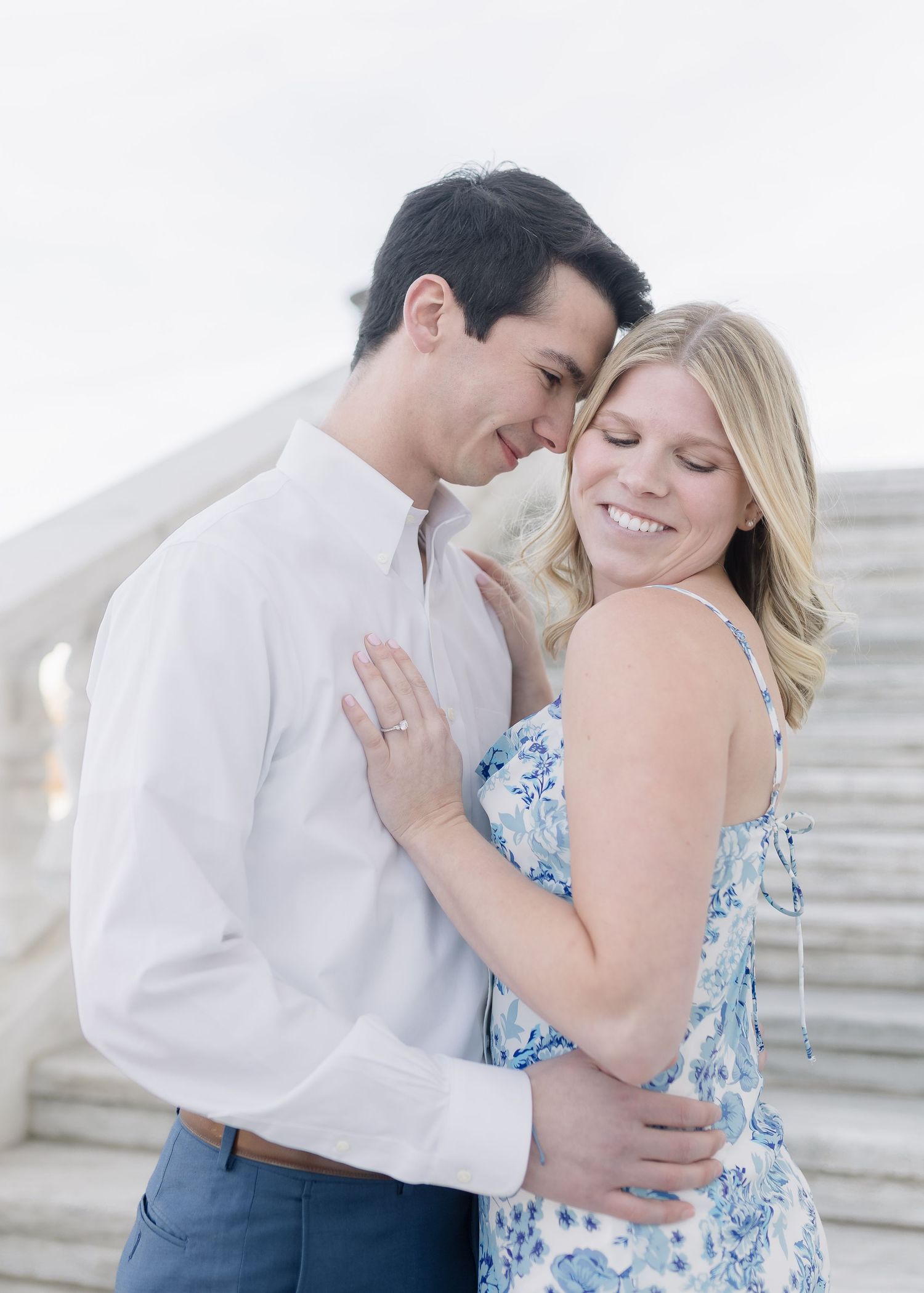 An intimate moment captured between a couple in white and floral blue attire against a light background.