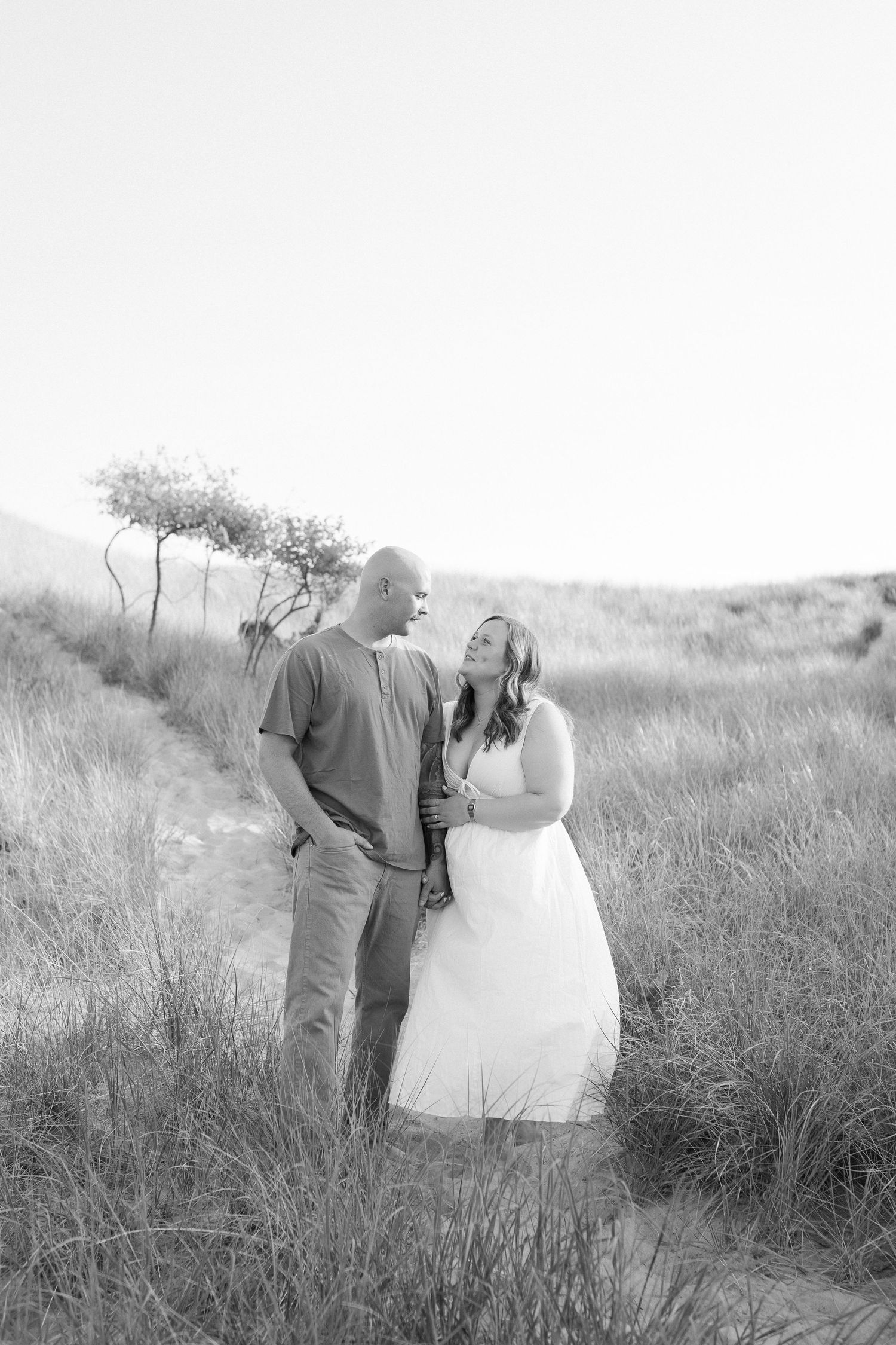A romantic black and white photo of a couple sharing a joyful moment together in a grassy field with trees in background.