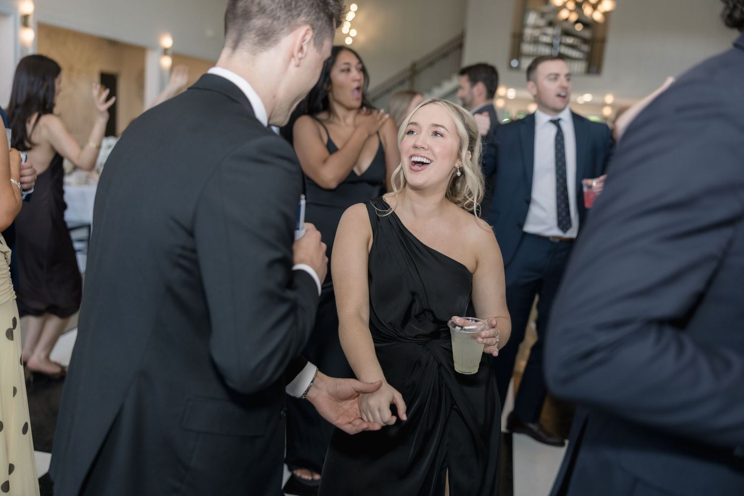 Guests in formal black attire laughing and socializing at an elegant evening event or wedding reception.