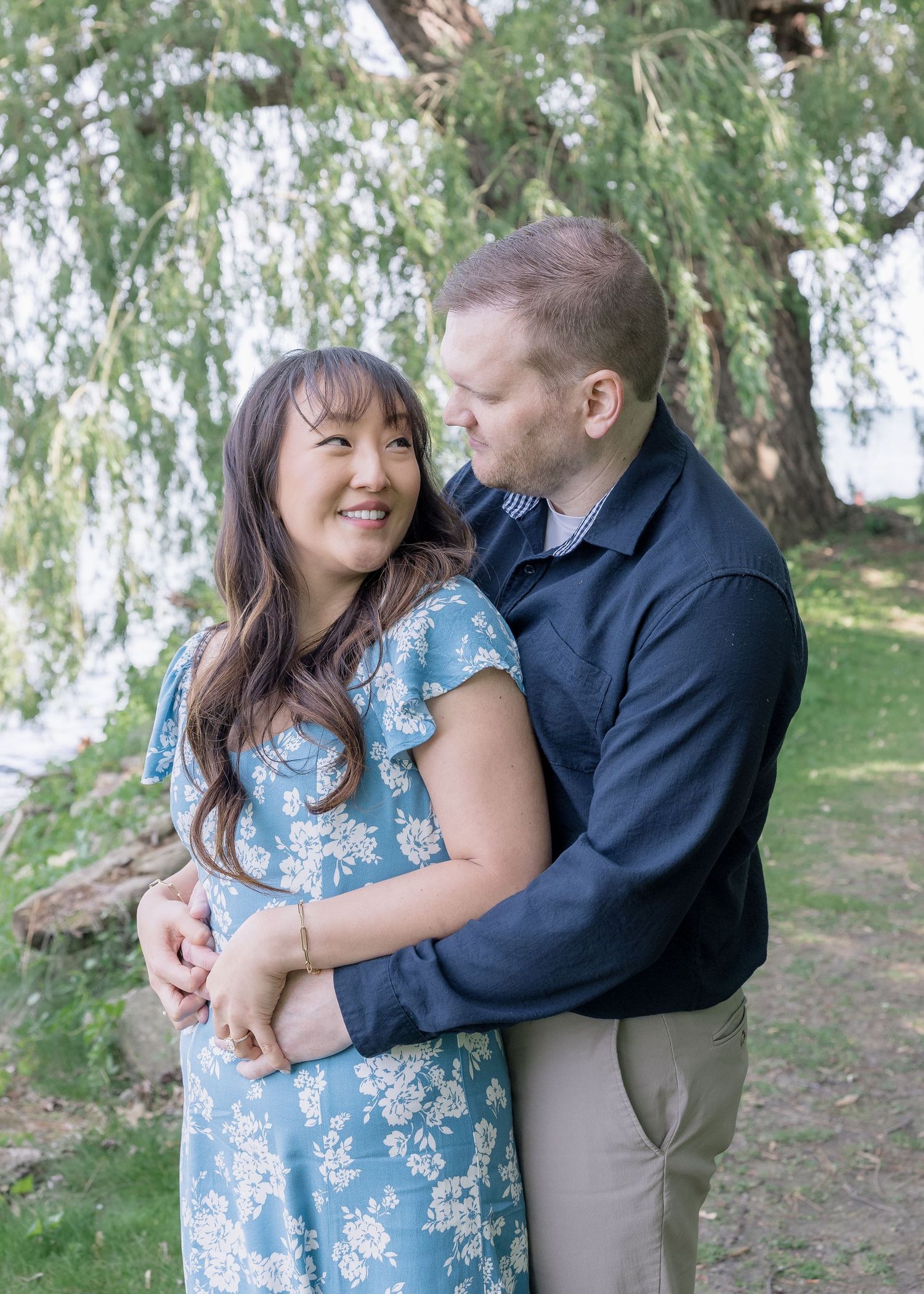Couple embracing under willow tree during outdoor photoshoot.