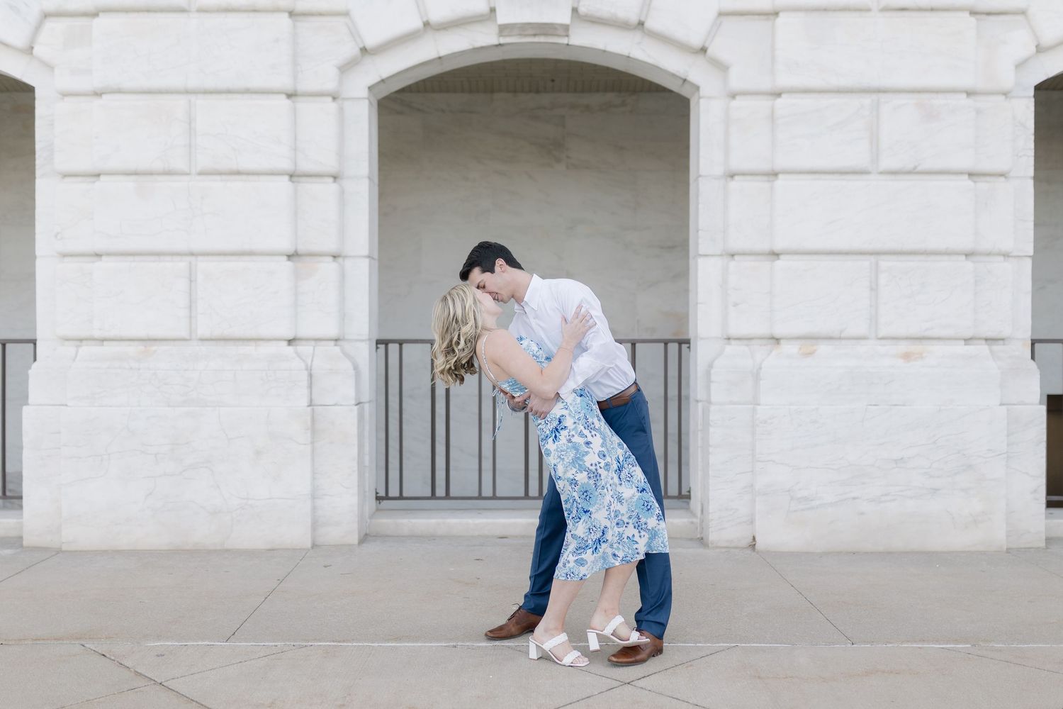 Couple poses romantically in front of a classic white stone building with archways.