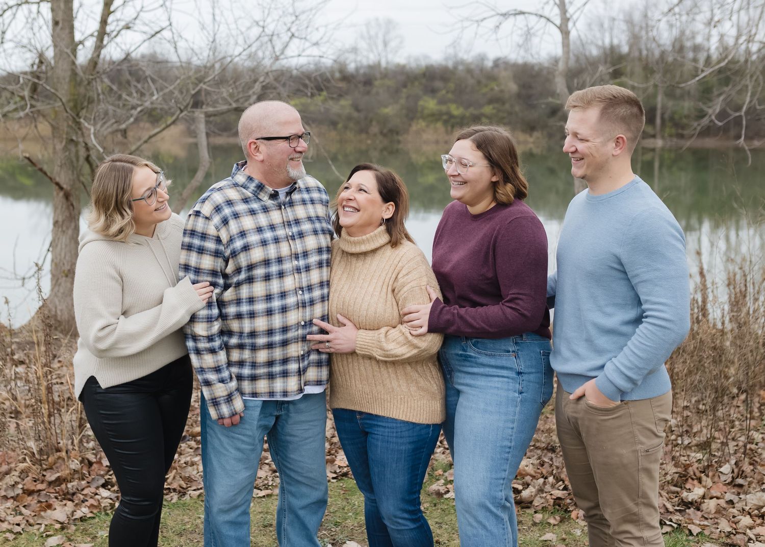 A group of people stand together by a lake in casual attire during fall, captured in multiple candid poses.