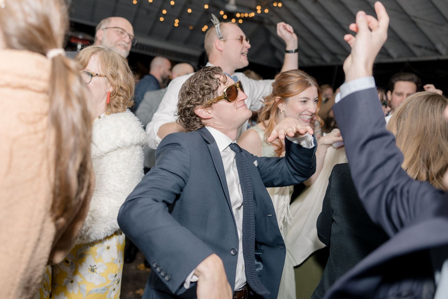 Energetic dance floor celebration at wedding reception with guests raising hands.