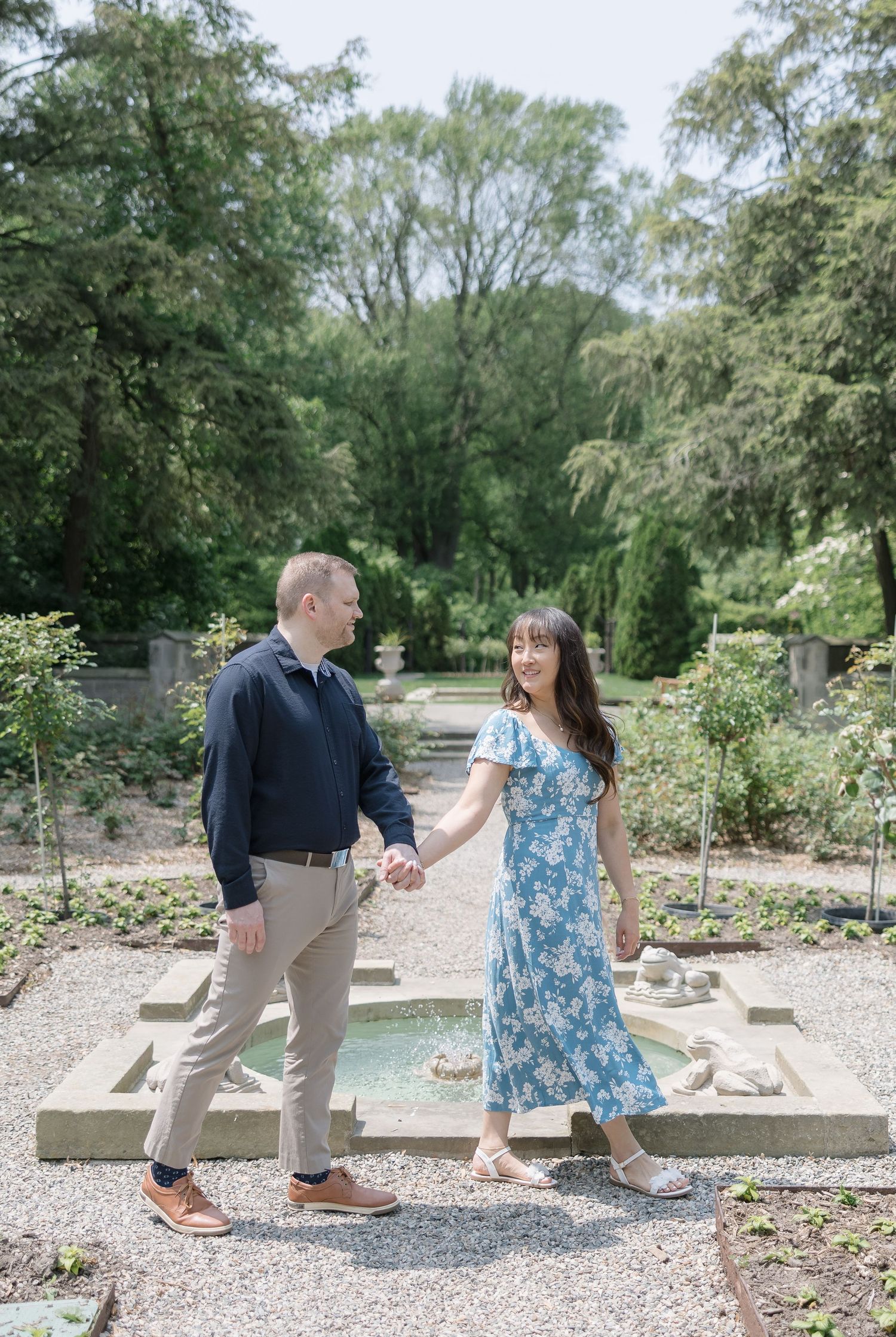 A couple interacts playfully on a stone bench in a landscaped garden with gravel paths.