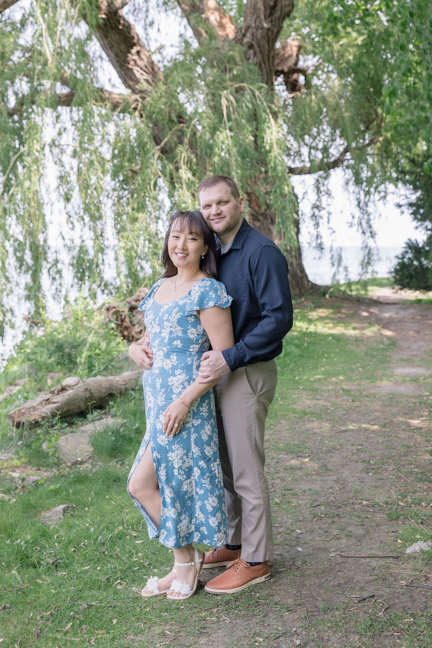 A couple shares loving moments under a weeping willow tree in a park setting.