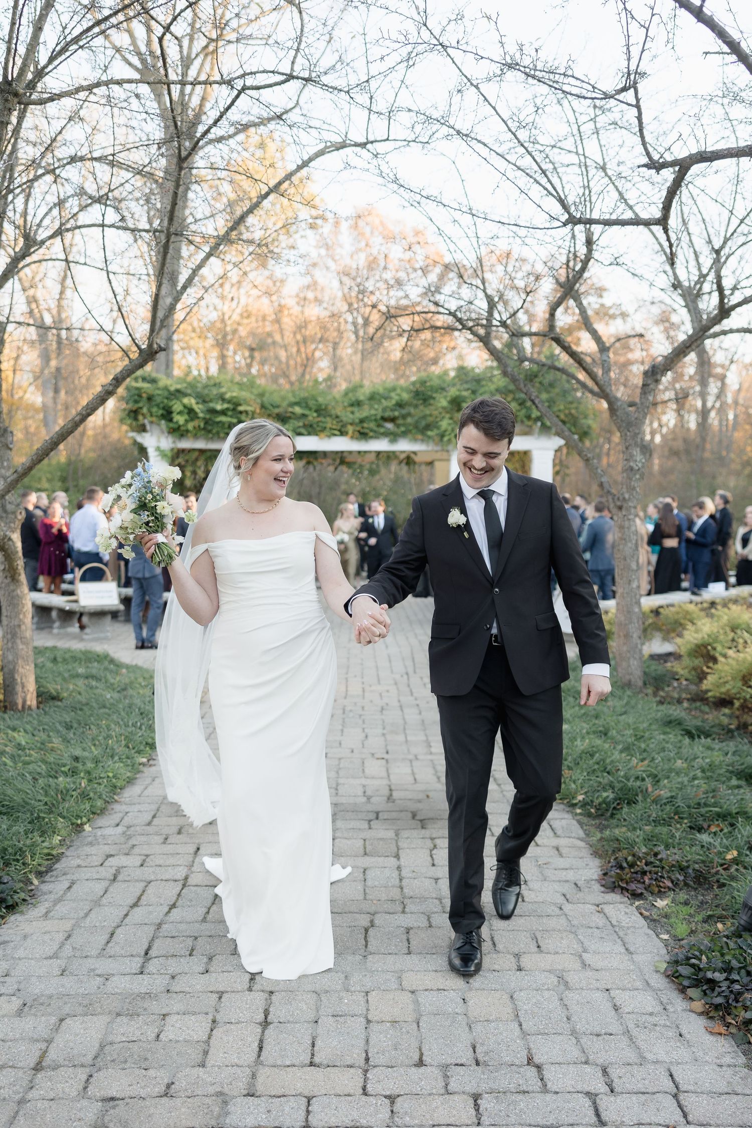 A wedding couple walking down a stone path surrounded by autumn trees.