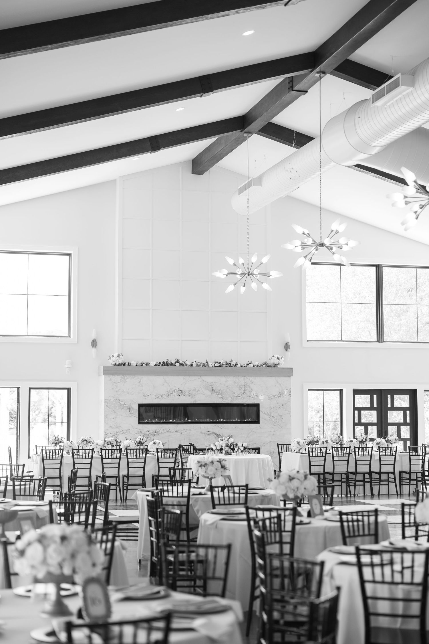 Elegant black and white wedding reception hall with vaulted ceilings, chandeliers, and round dining tables.