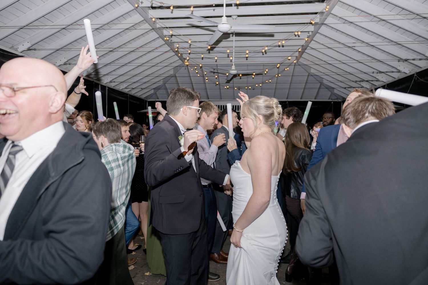 Wedding party dancing and celebrating under a white tent ceiling.