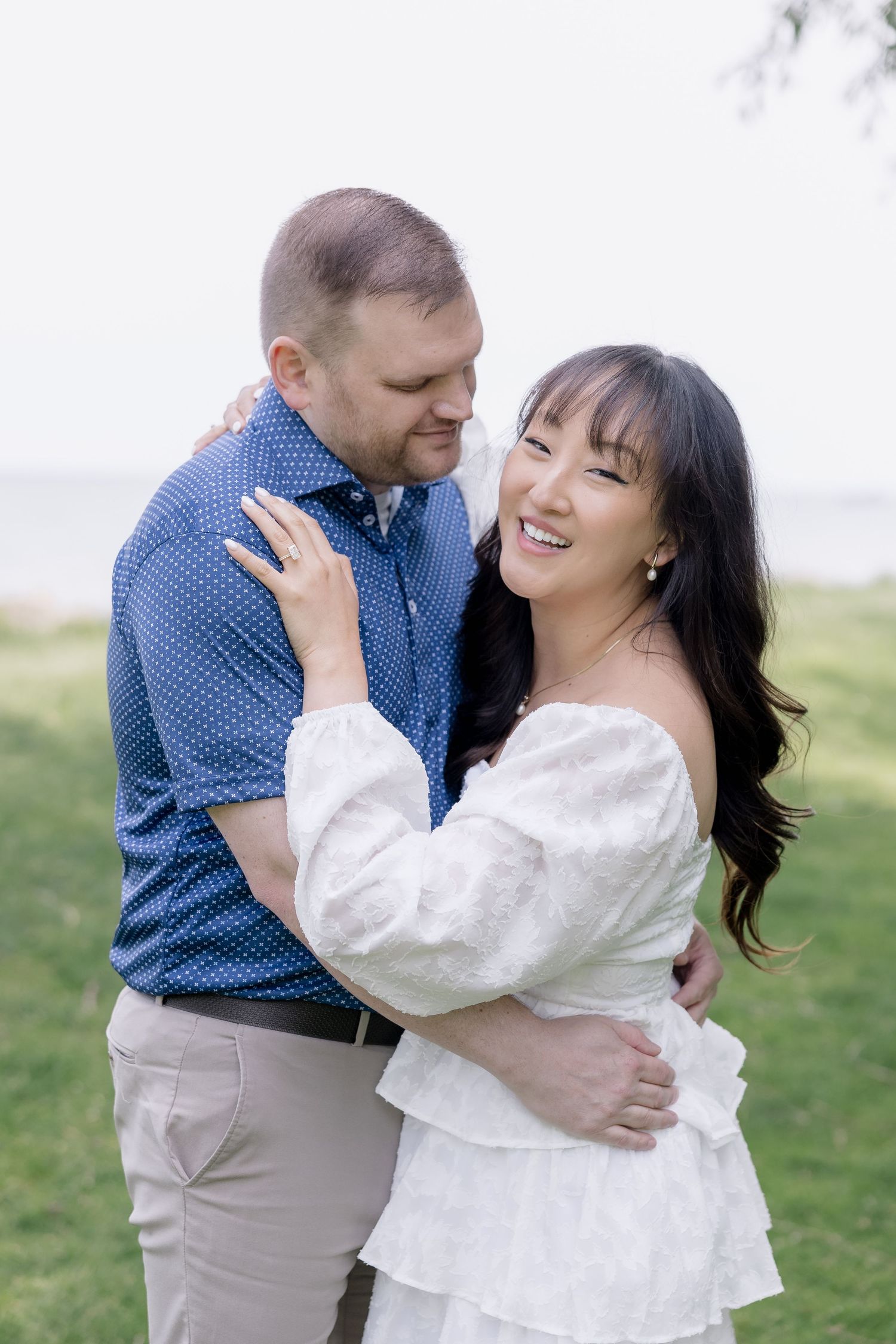 A couple embraces in a romantic outdoor photo session wearing blue and white outfits against a natural background.